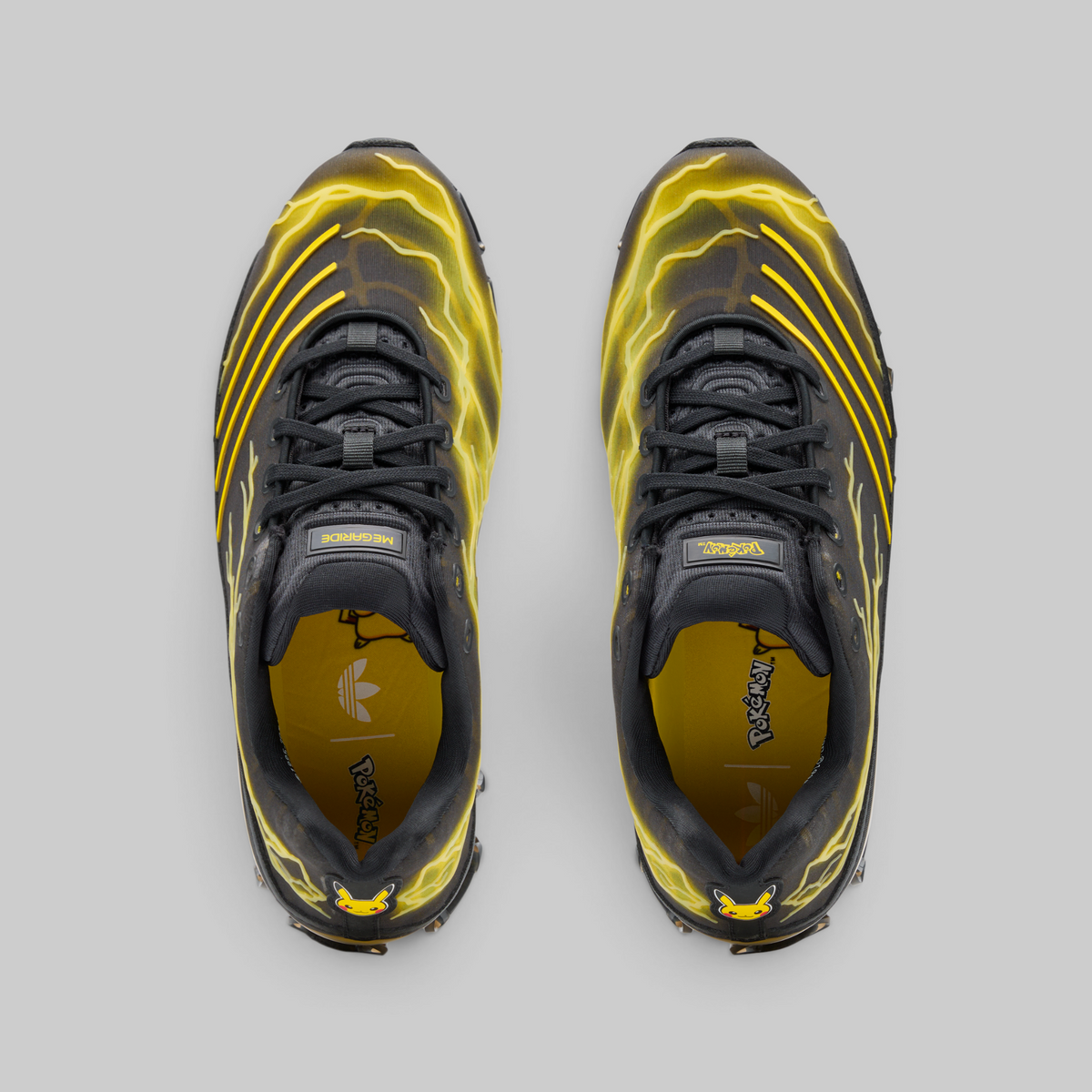 A pair of Adidas Originals Superstars sneakers shown from a top-down view, featuring a black and yellow colorway with a yellow lightning-bolt pattern on a gray background.