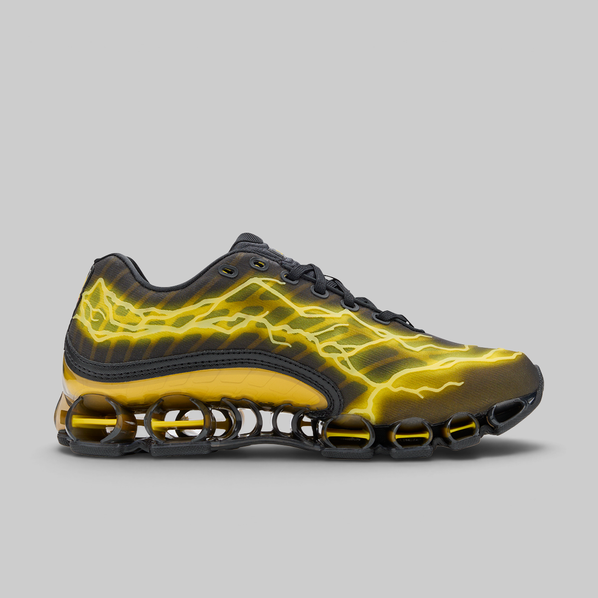 A Nike Shox sneaker in black with a vibrant yellow lightning-bolt pattern across the upper, shown in a side profile on a solid gray background.