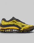 A Nike Shox sneaker in black with a vibrant yellow lightning-bolt pattern across the upper, shown in a side profile on a solid gray background.
