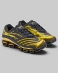 A pair of Nike Air Max 90s sneakers in black with vibrant yellow lightning-bolt graphics and a gold-toned cushioned sole, displayed on a neutral gray background.