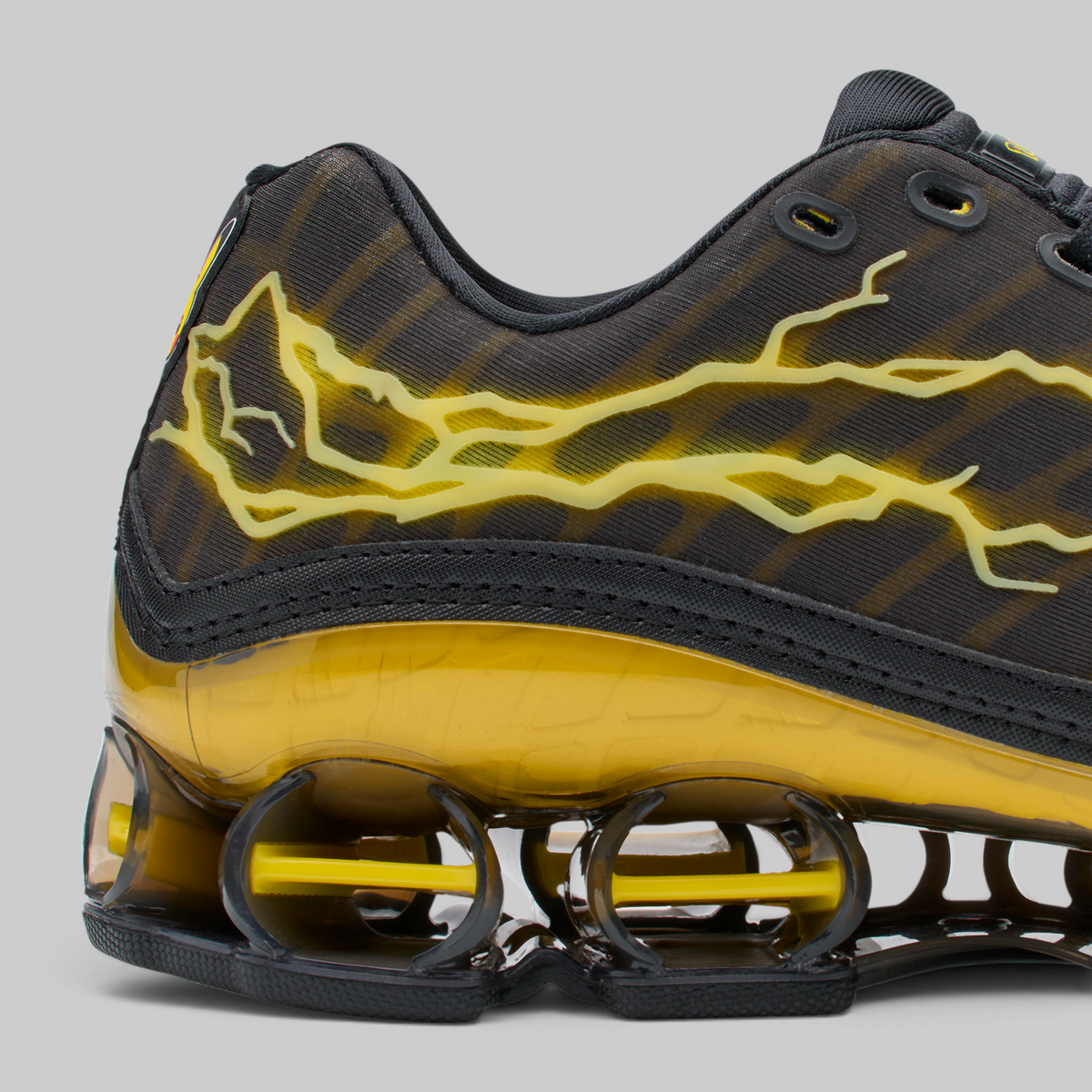 Close-up of a black and yellow athletic sneaker showing the side panel with a yellow lightning-bolt graphic, the translucent yellow midsole, and the black and yellow Shox sole.