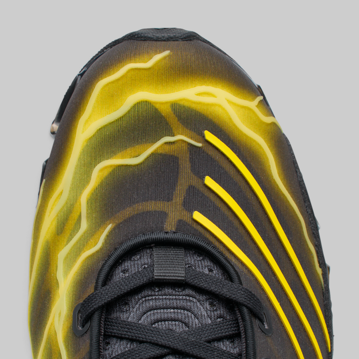 Close-up of a black athletic shoe with bright yellow lightning-bolt style graphics on the upper, shown against a light gray background.