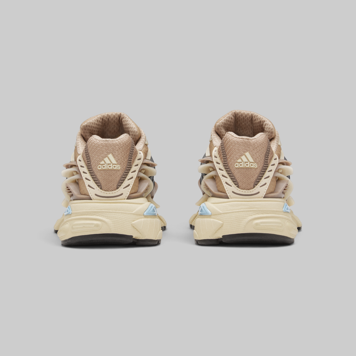A pair of Adidas Pharrell Williams Adistar Jellyfish - "Crystal Sand" sneakers shown from the back, featuring a chunky beige and tan design with a textured leather heel tab and light blue geometric accents on the midsole.