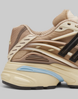 A close-up side profile of Pharrell Williams Adistar Jellyfish - "Crystal Sand" a chunky sneaker in beige and cream with black side stripes and a light blue accent on the midsole, set against a solid gray background.