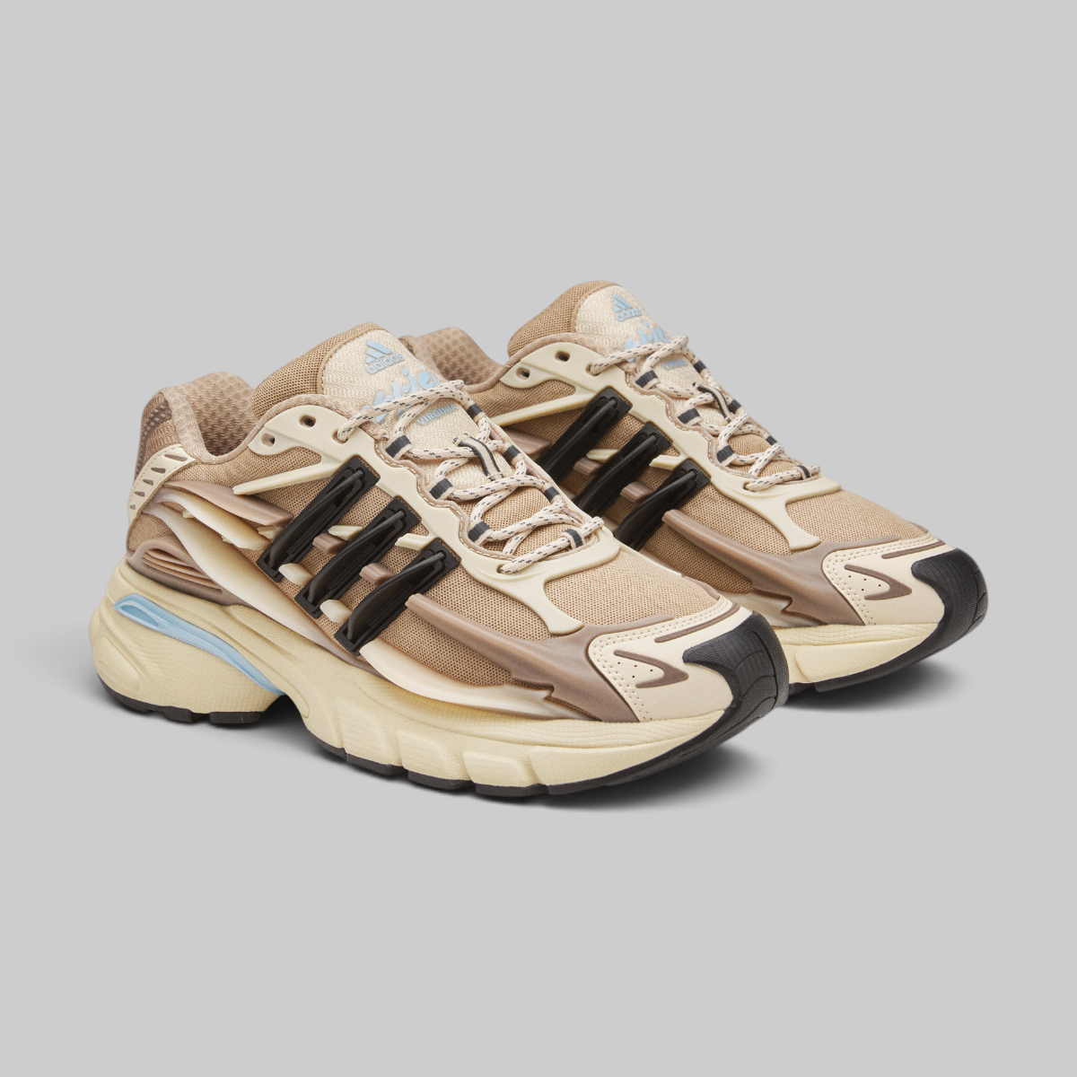 Pharrell Williams Adistar Jellyfish - "Crystal Sand" sneakers in beige, tan, and cream with black side accents and light blue details, photographed on a solid gray background.