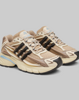 Pharrell Williams Adistar Jellyfish - "Crystal Sand" sneakers in beige, tan, and cream with black side accents and light blue details, photographed on a solid gray background.