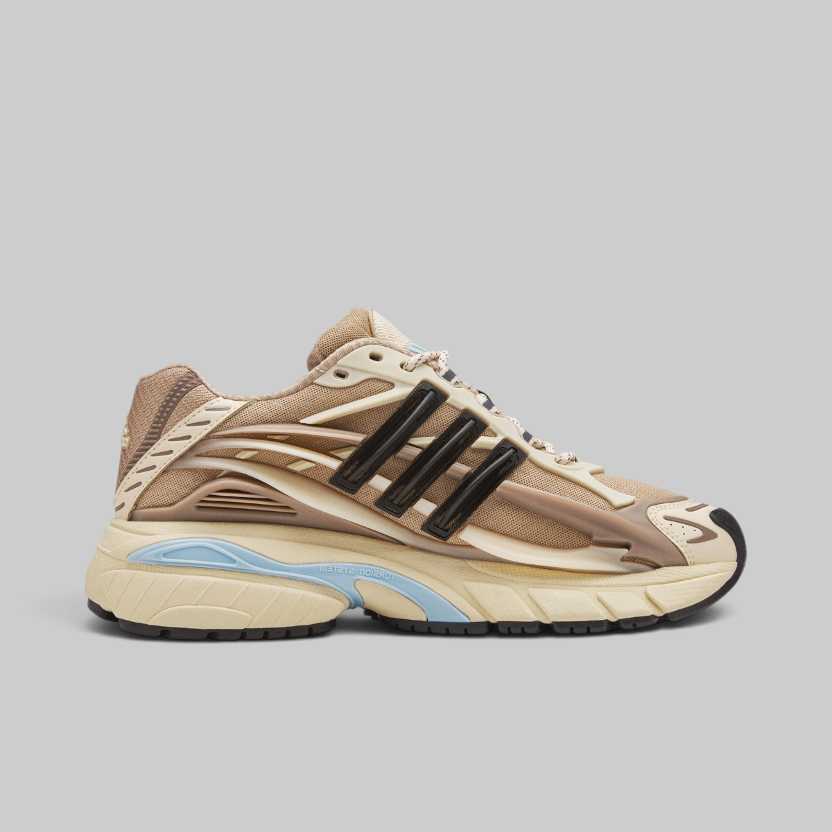 Pharrell Williams Adistar Jellyfish - "Crystal Sand" sneaker in beige, cream, and brown with black three-stripes and a light blue accent on the midsole, shown against a solid gray background.