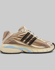 Pharrell Williams Adistar Jellyfish - "Crystal Sand" sneaker in beige, cream, and brown with black three-stripes and a light blue accent on the midsole, shown against a solid gray background.