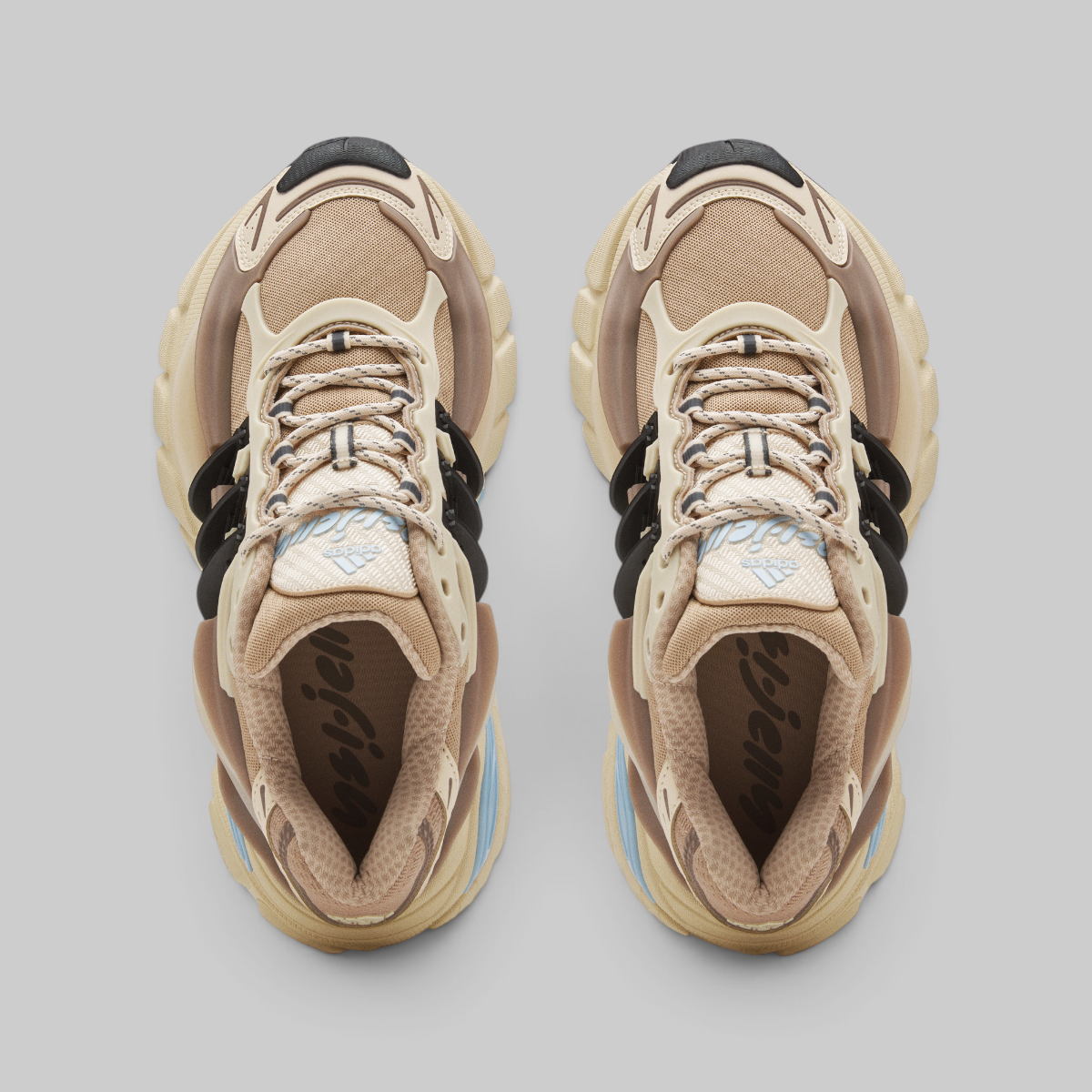 A pair of Pharrell Williams Adistar Jellyfish - "Crystal Sand" sneakers shown from a top-down view on a light gray background. The shoes feature a beige and tan color palette with black accents on the laces and heel areas, and subtle light blue details on the tongue and midsole.