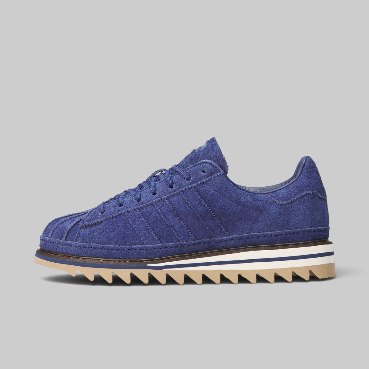 A single blue suede sneaker with a chunky, jagged gum sole, photographed from the side against a solid light gray background.