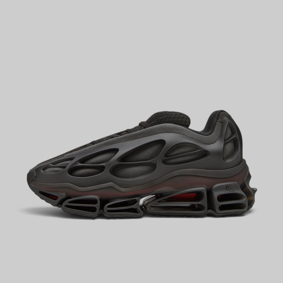A black Nike sneaker with a distinctive hollow, bubble-like upper and a translucent dark red midsole cushioning system, shown in a side profile on a light gray background.
