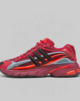 A red Adidas sneaker with black three-stripes, a translucent light blue side panel, and a bright orange midsole accent, shown in profile against a light gray background.