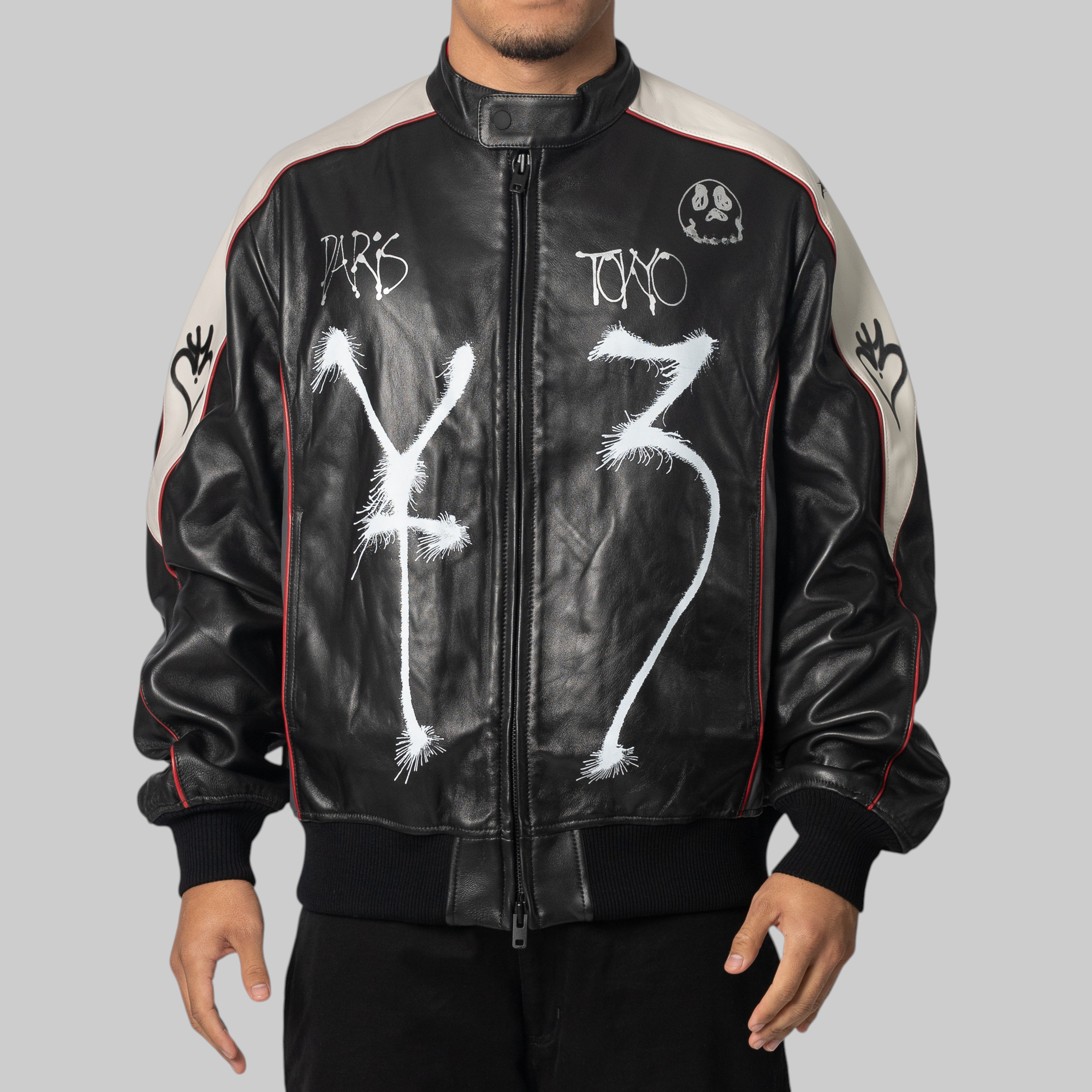 Y-3 x Chito black leather bomber jacket with white graffiti-style graphics, red piping, and beige shoulder panels, photographed against a solid gray background.