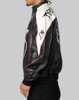 A side-profile view of a person wearing a black and white leather jacket with red piping and graphic designs on the back and shoulders, paired with black pants, against a solid gray background.
