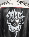 Close-up of the back of a black leather jacket with a large white skull graphic, a cream shoulder yoke with black distressed lettering, and a thin red piping detail.