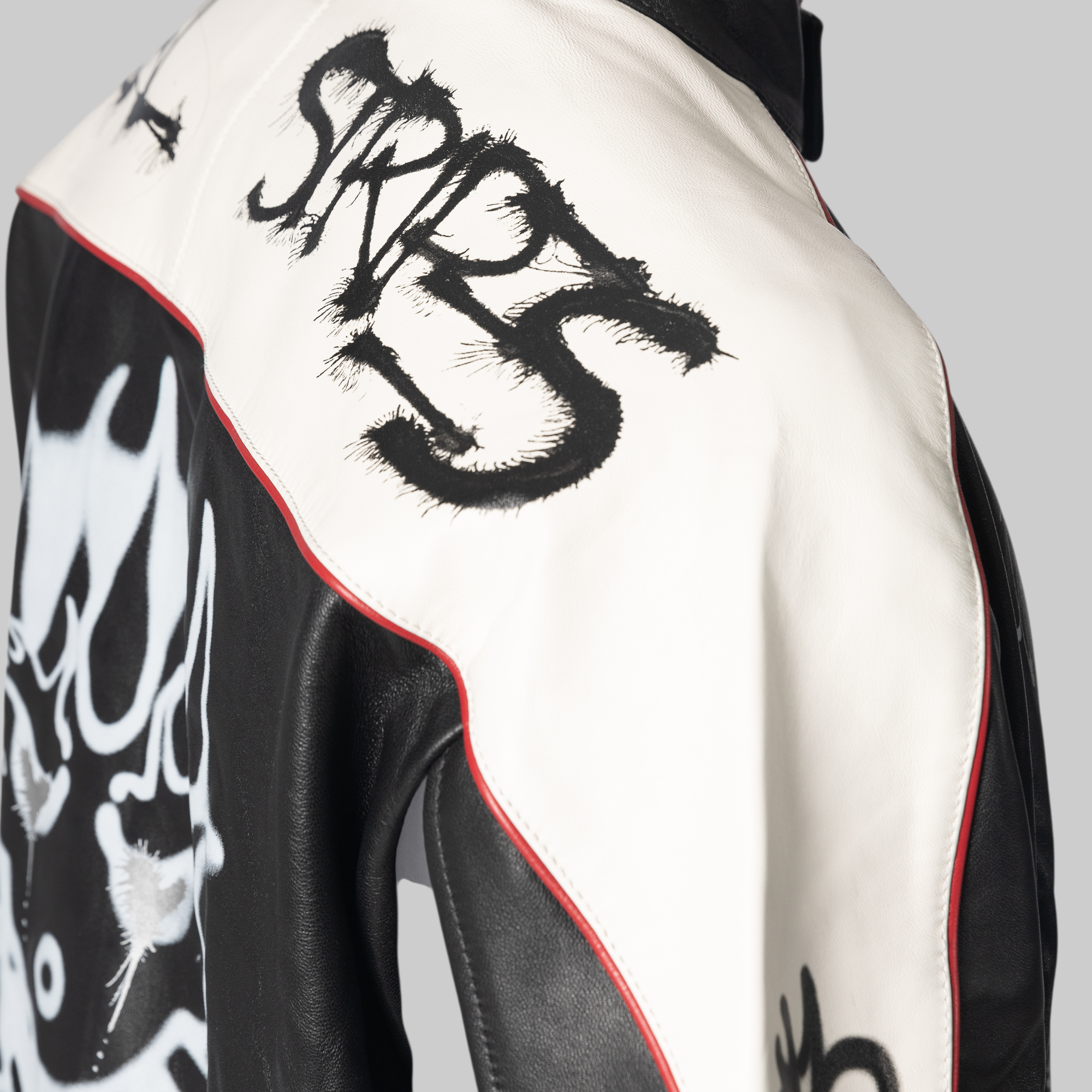 Close-up of a black and white leather jacket with red piping, featuring a large black graffiti-style 'SRT 5' graphic on the shoulder and a white skull graphic on the side.