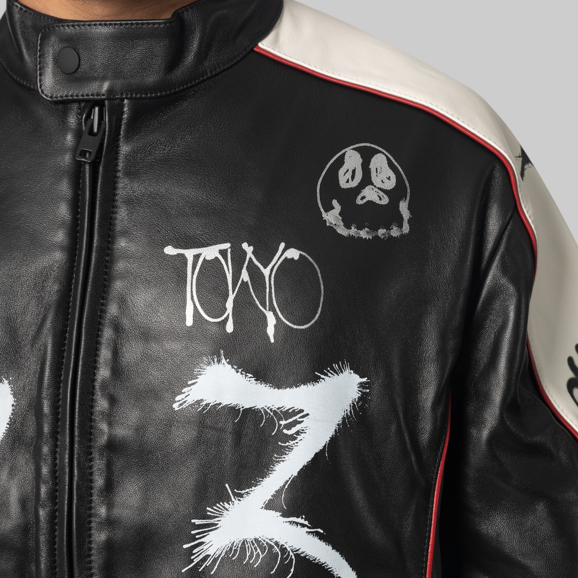 Close-up of a black leather jacket with white graphic artwork, including the word 'Tono' and a skull design, with off-white shoulder panels and thin red piping.