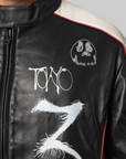 Close-up of a black leather jacket with white graphic artwork, including the word 'Tono' and a skull design, with off-white shoulder panels and thin red piping.
