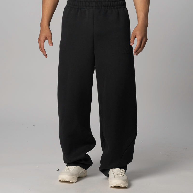 Black wide-leg sweatpants worn by a model, paired with white sneakers, shown from the waist down against a light gray studio background.
