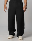 Black wide-leg sweatpants worn by a model, paired with white sneakers, shown from the waist down against a light gray studio background.