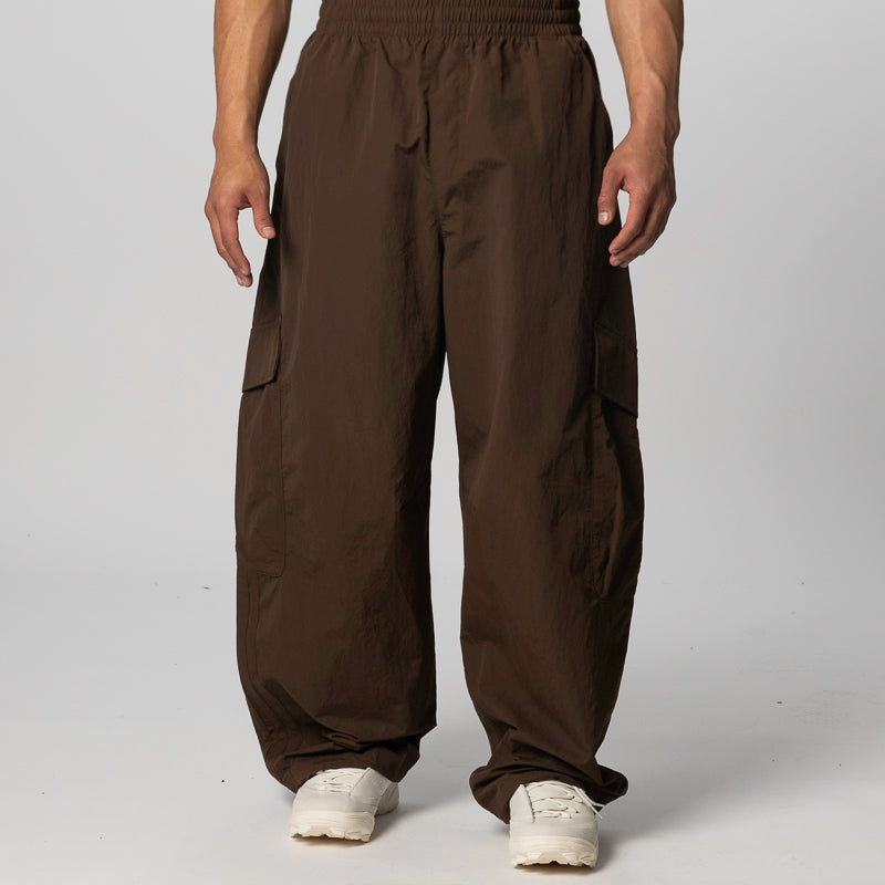 A person wearing loose, wide-leg brown cargo pants with an elastic waistband and white sneakers, photographed against a light gray studio background.