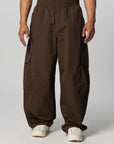 A person wearing loose, wide-leg brown cargo pants with an elastic waistband and white sneakers, photographed against a light gray studio background.