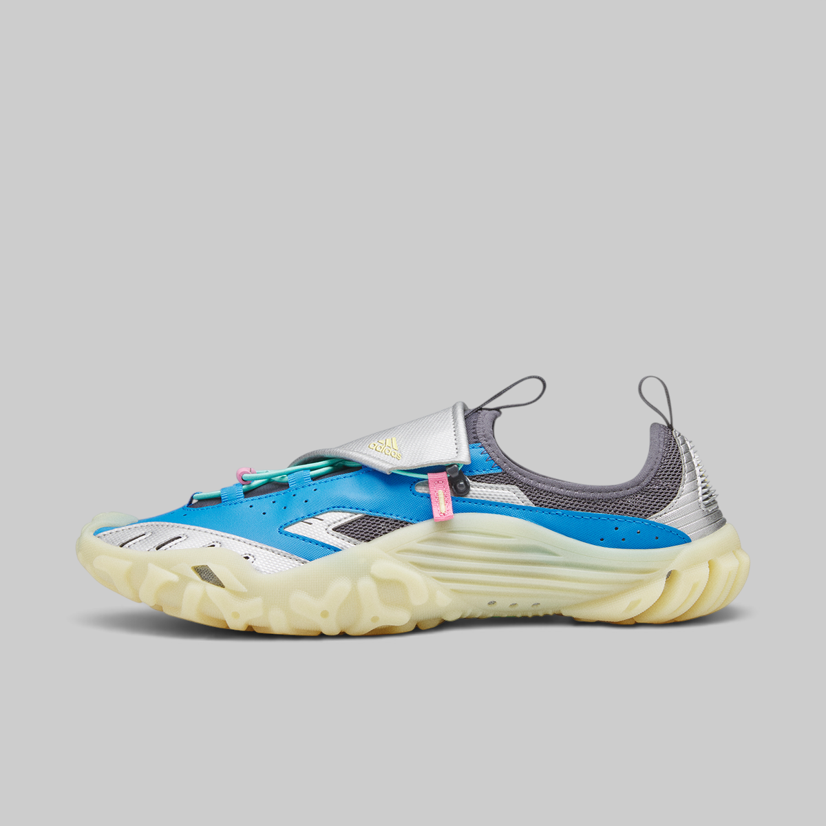 A single athletic sneaker shown in profile against a solid gray background. The shoe features a bright blue upper, a white strap with a silver buckle, a gray mesh collar, and a thick, textured cream-colored sole.