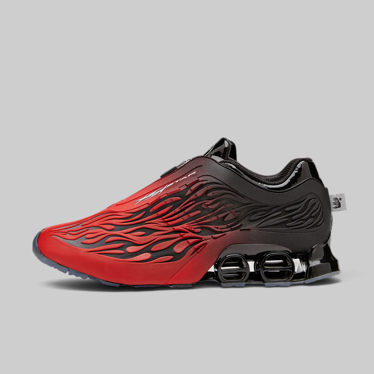 A red and black athletic sneaker with a flame-like pattern on the upper, black laces, and a prominent black cushioning system on the sole, shown against a solid gray background.