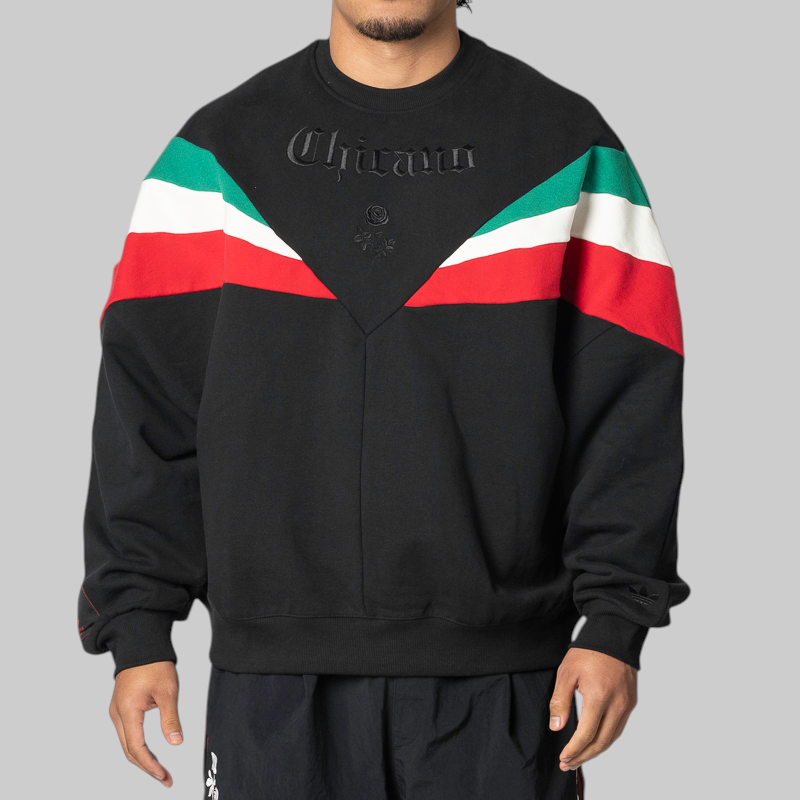 A man wearing a black crewneck sweatshirt with green, white, and red color-blocked shoulder stripes and embossed 'Chavarria' lettering on the chest, photographed against a solid gray background.
