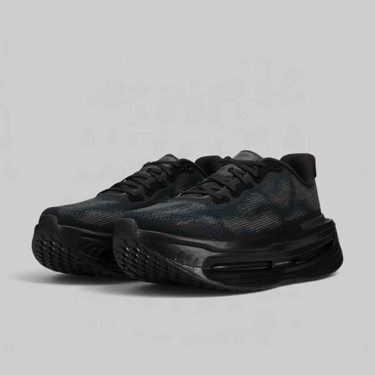 A pair of black athletic sneakers with a textured knit upper and thick cushioned soles, photographed on a light gray background.