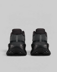A pair of Nike sneakers shown from the back, featuring dark gray and black mesh and synthetic materials with chunky black soles, set against a solid light gray background.