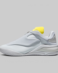 A white and light gray athletic sneaker with a bright yellow heel tab, shown in a side profile on a solid gray background.