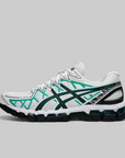 A white ASICS sneaker with dark green and teal accents, featuring the brand's signature stripe design, shown in a side profile on a solid gray background.