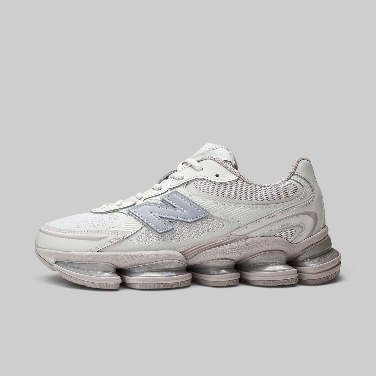 A New Balance sneaker in off-white and light gray, featuring a chunky, multi-layered gel-like sole, shown from a side profile on a solid gray background.