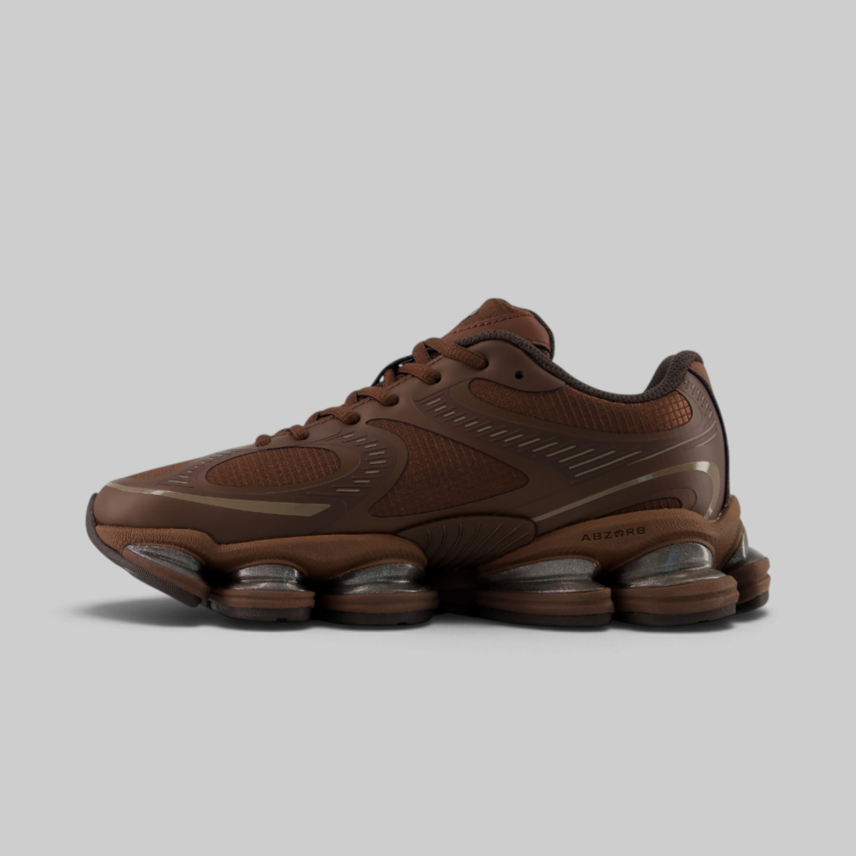 A single brown athletic sneaker shown in a side profile against a solid light gray background. The shoe features a textured brown upper with subtle metallic bronze accents, matching brown laces, and a distinctive multi-bulb translucent sole.