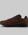A brown New Balance sneaker with a dark gray 'N' logo and black sole, shown in a side profile on a light gray background.